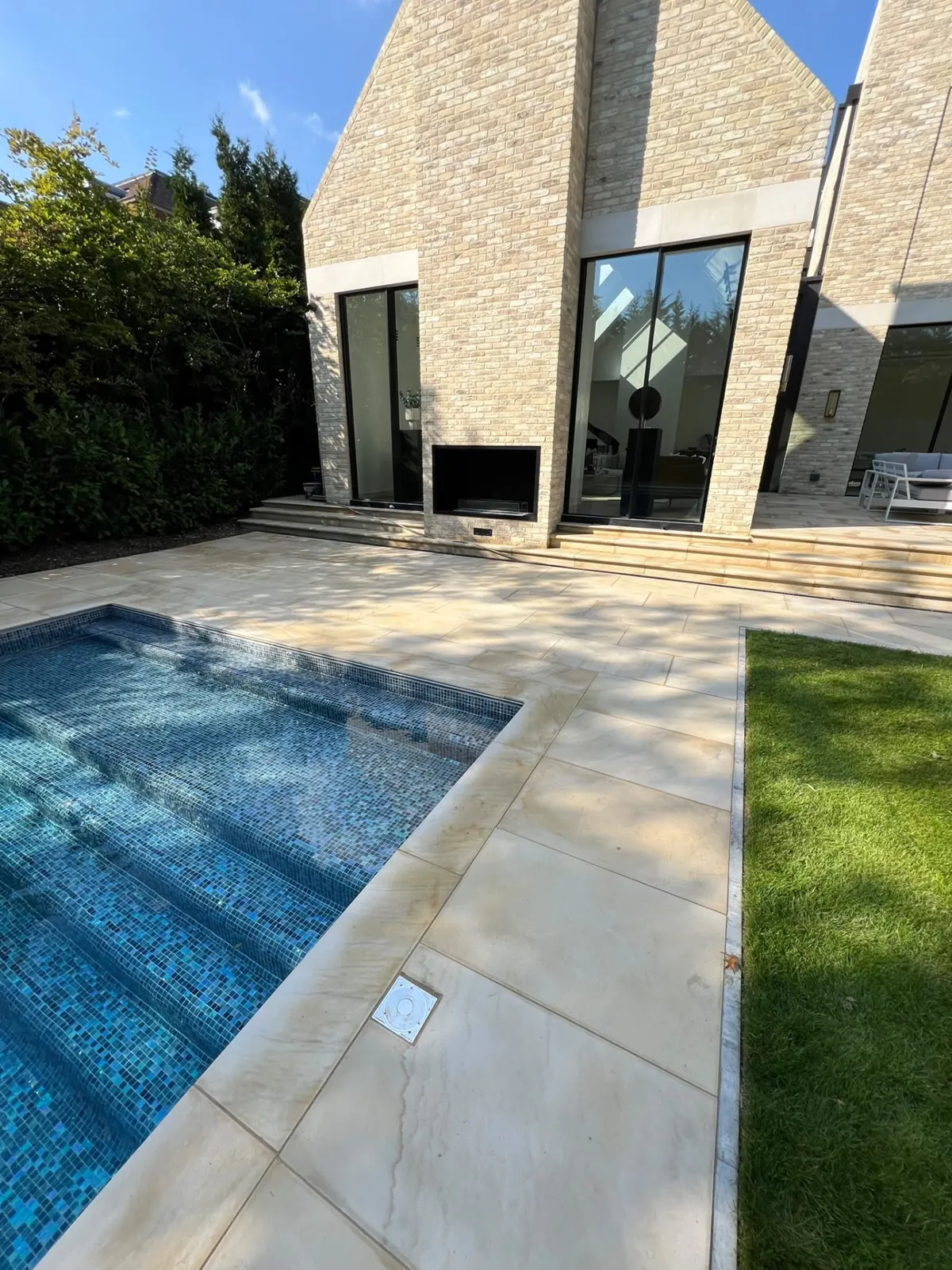 Large format sandstone pool surround and patio with steps to a modern home